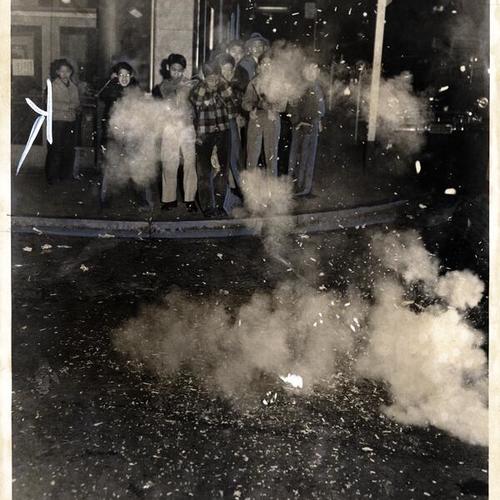 [Group of people stand and watch as fire crackers explode on New Years, in Chinatown]