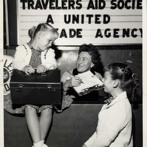 [Travelers Aid Society volunteer and two children at Travelers Aid Society of California desk]
