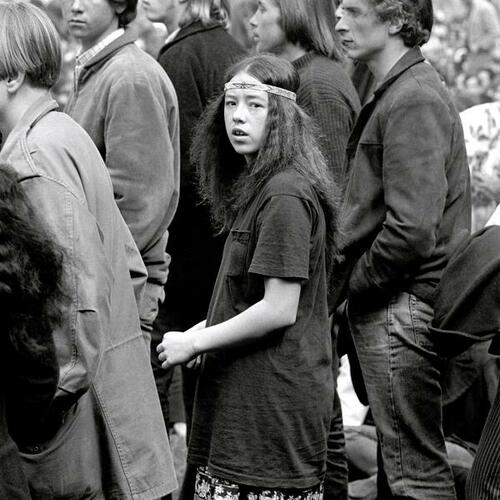 [Teenaged girl stands alongside several older young men at a summer music festival]