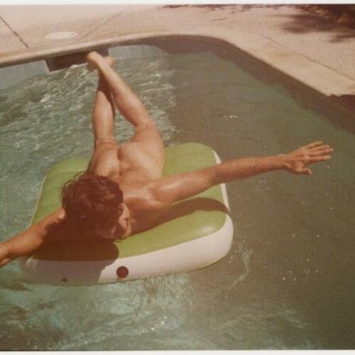 Ken Maley, nude, laying on inflatable in pool at Rock Hudson's Palm Springs home