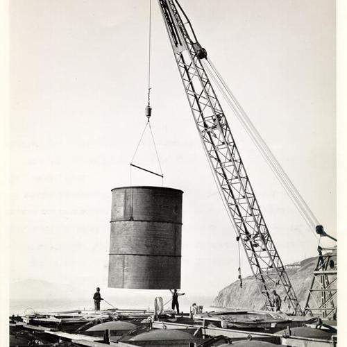 [View of cylinder being lowered into place to be welded on one of the 28 cylinders of Caisson No. 6 for San Francisco-Oakland Bay Bridge pier]