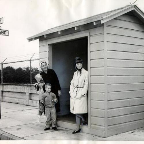 [Mrs. James Mazzaferro, her son Mark, and Pat Kurpinsky standing at a Municipal Railway shelter at University and Wayland streets]