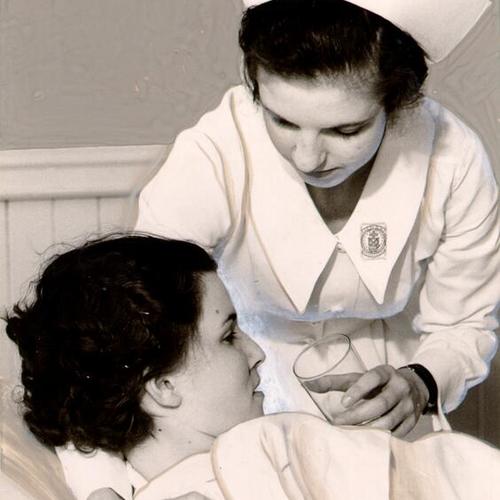 [Unidentified graduate of Mary's Help School of Nursing helping a patient]