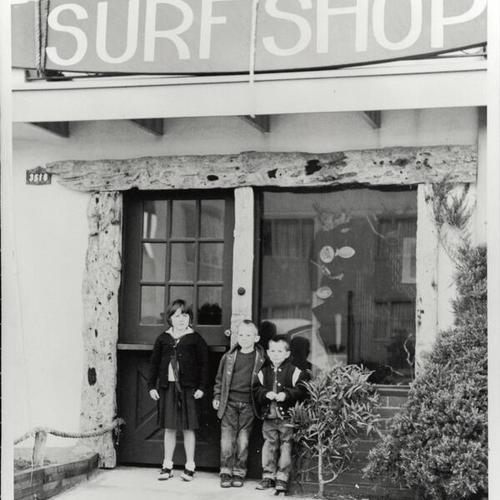 [Jack O'Neill's first surf shop on Wawona Street with Jack's children, Cathy, Mike and Pat, standing in front of shop]