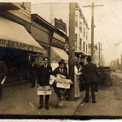 [Pete Rielly and Eddie Campi selling newspapers in front of Abraham's Pharmacy, 1198 McAllister Street, at Fillmore]