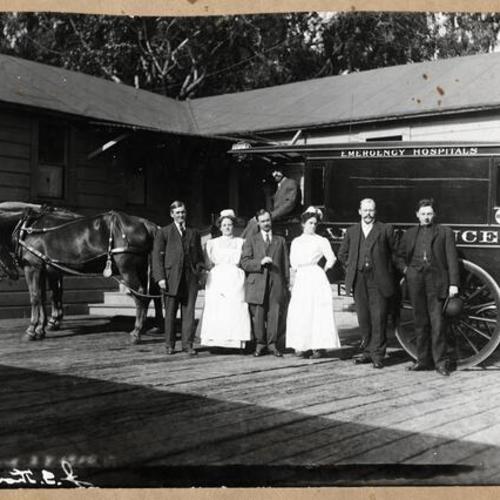 [James O'Dea, nurse Annie Andrew, Dr. Fred Zumwalt, nurse Theresa Gile, Charles Bucher, Father William Sullivan and John Thoma on ambulance before the temporary Central Emergency Hospital in Jefferson Square]