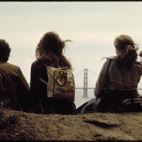 Three people sitting in view of Golden Gate Bridge