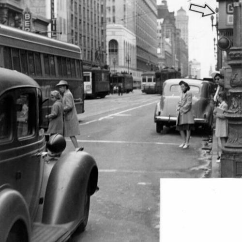 [Two young girls jaywalking on Market Street are sandwiched between automobiles and streetcars]