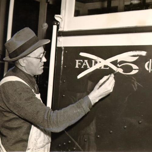 [Oscar W. Larsen painting over the five cent fare sign on the side of a Municipal streetcar]