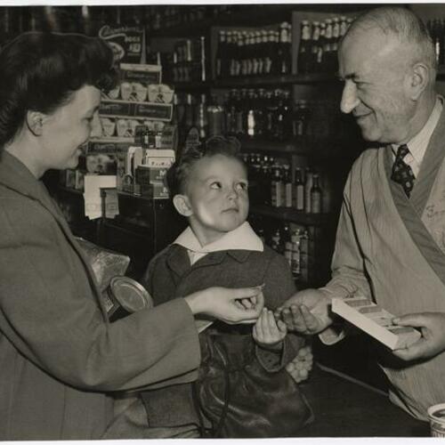 Mrs. V. K. Brown and her son Jimmy getting a ration token from Grocer Bagus Arman