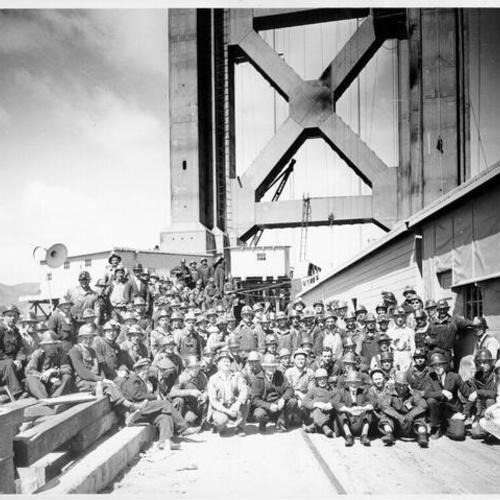[Workmen being photographed in front of Golden Gate Bridge tower]