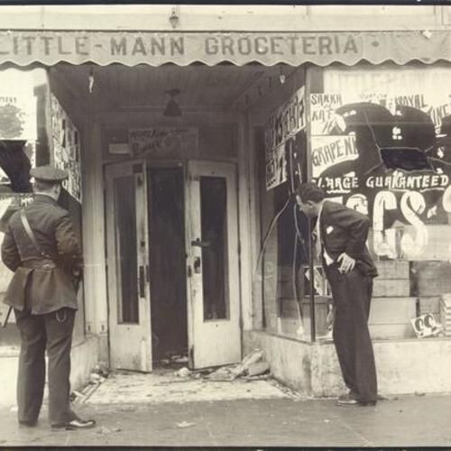 [Police officer and man examining Little-Mann grocery store damaged by thrown rocks during dock strike]