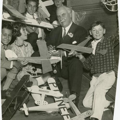 [Mayor James Rolph, Jr. sitting with a group of children holding model airplanes]
