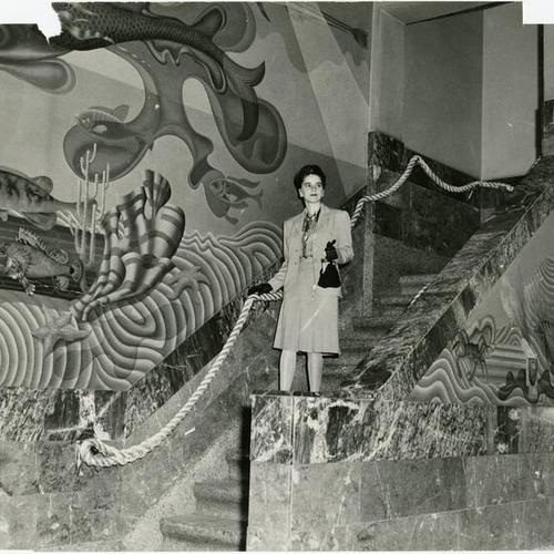 [Beverley Waldo stands on the staircase under the huge and elaborate murals depicting the story of the lost continent of Atlantis, in the Maritime Museum]