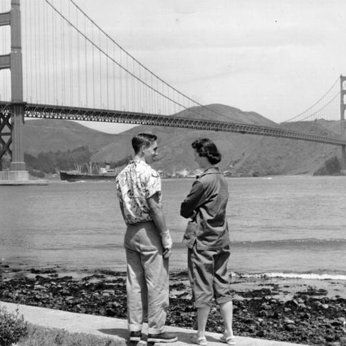 [Idaho tourists, Dwane Hodgson and Carol Lyle, standing on the beach near Fort Point and Golden Gate Bridge in the background]