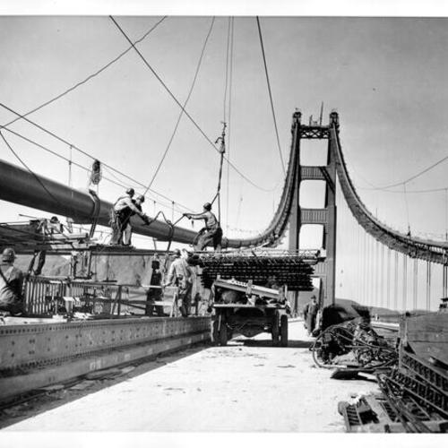 [Workmen tearing catwalk construction of Golden Gate Bridge from the west cable on the San Francisco side]