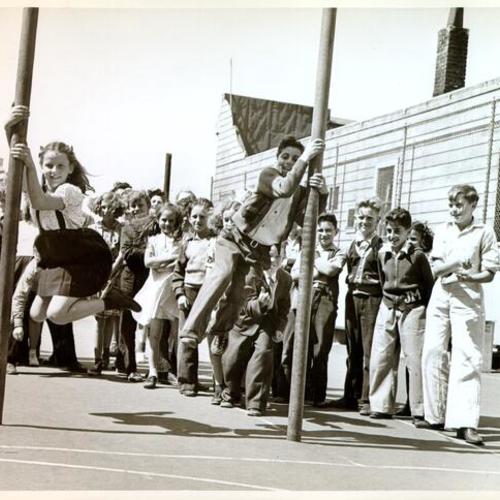 [Children swinging on poles in the playground at John Muir School]