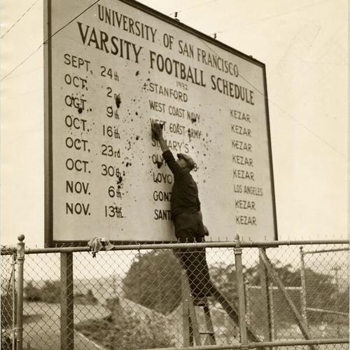 [Worker washing sign displaying the University of San Francisco varsity football team schedule]