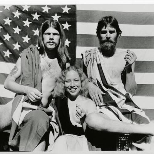 [In the Spirit of 1976, Frank, Denise and unknown friend posing with American flags and smoking joints]
