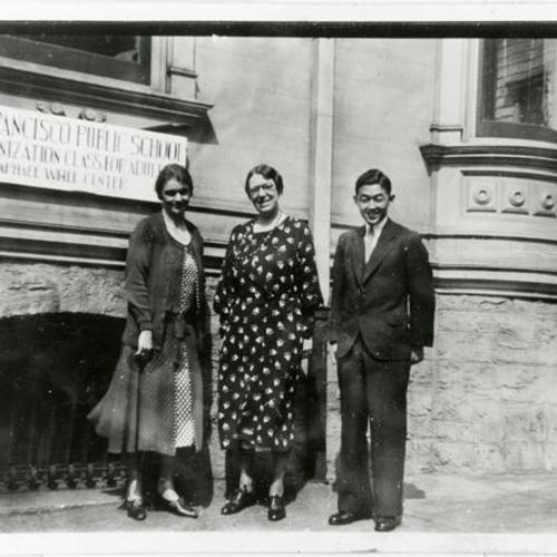 [Two teachers and a man standing in front of "Americanization Class for Adults" sign at 1223 Buchanan Street in 1934]