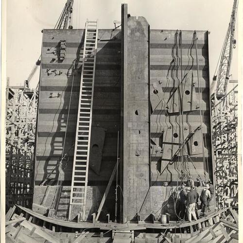 [Workmen fitting a prefabricated unit into the bottom hull of a ship]