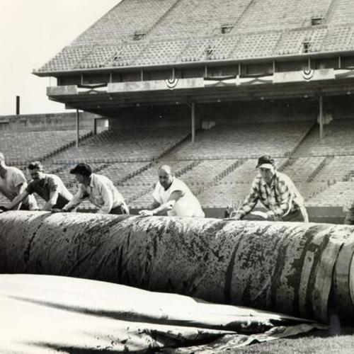 [Construction workers rolling up tarpaulin at Candlestick Park]