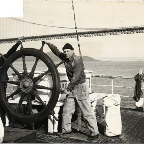 [Crew members L. A. (Obie) Oberauer and Herb Madden standing at the helm of the sailing ship "Pacific Queen" (also known as the "Balclutha")]