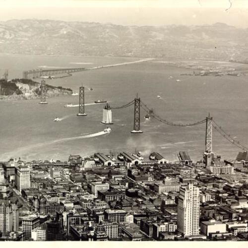 [Aerial view of catwalks being extended to each support tower of the San Francisco-Yerba Buena Island section of the Bay Bridge, with the cantilever section of the bridge from the island to Oakland visible in the background]