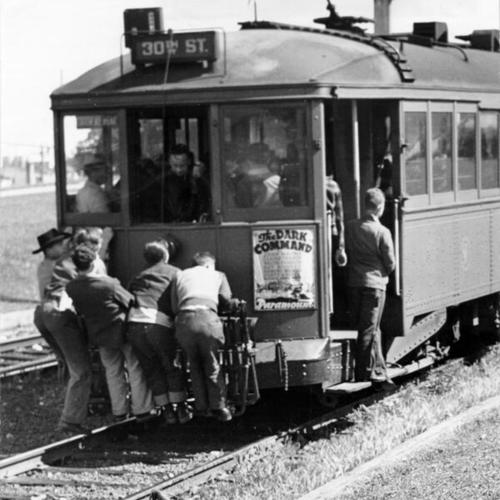 [Mission High School students riding on the rear bumper of a streetcar]
