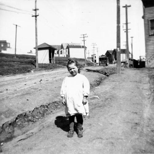 [Young girl standing on Chenery Street at Castro, with streetcar in background]
