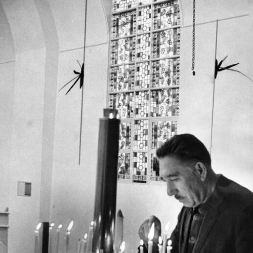[Serge Mironoff, assistant warden, with stained glass window behind him at the Holy Virgin Cathedral]