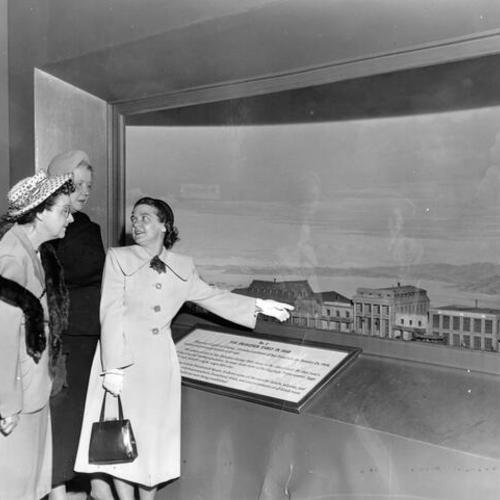 [Mrs. Kenneth R. MacDonald pointing out features of a historic diorama of San Francisco to Mrs. Carl H Kiefer and Mrs. G.P. Swenson]