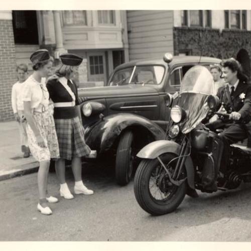 [Patrolwoman sits on her three wheeled motorcycle while talking with young people]