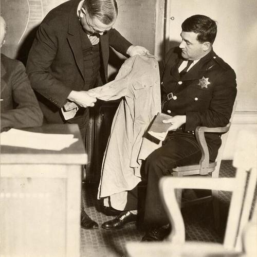 [Coroner T.B.W. Leland and Officer Ed Woods inspecting a jacket]