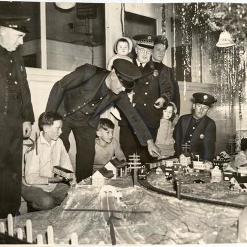 [Fire Chief Brennan and children standing around the miniature village and a huge christmas tree at Engine 24]