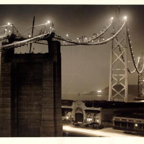 [Nighttime view of lighted Bay Bridge catwalks during construction of San Francisco section]