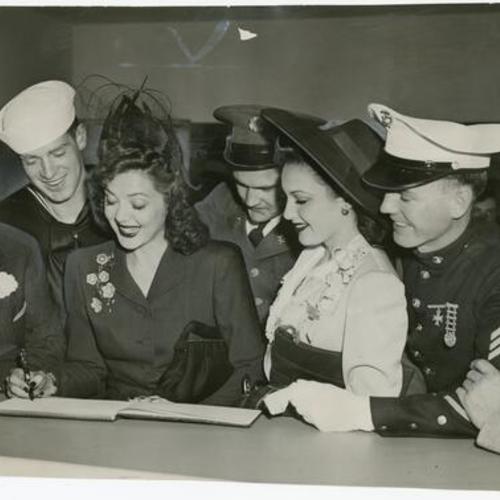 [Ann Rutherford signs register at Hospitality House with Mayor Angelo Rossi, military personnel and civilians watching]