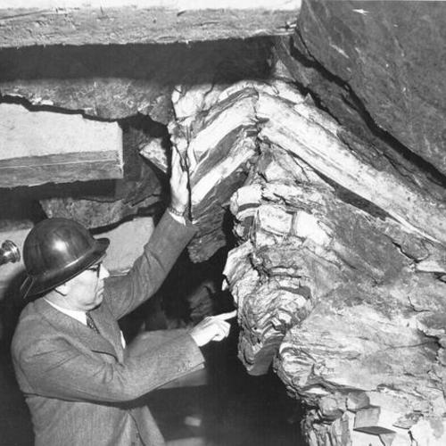 [C.H. Purcell, Chief Engineer, pointing at rock inside the tunnel on Yerba Buena Island during San Francisco-Oakland Bay Bridge construction]