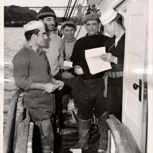 [Coast Guardsman checking the identification cards of crew members on a fishing vessel at the San Francisco waterfront]