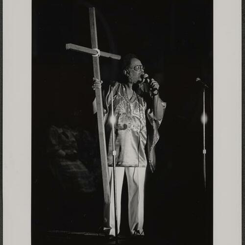 Reverend Cecil Williams holding wooden cross to break a rock (symbolic of crack cocaine) on Easter