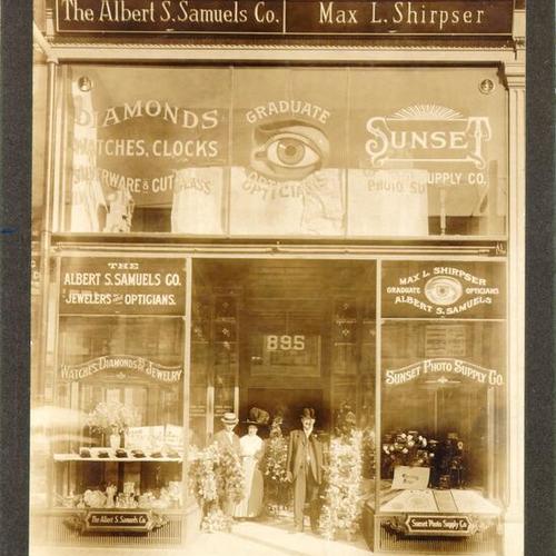 [Three unidentified people standing at the entrance to Albert S. Samuels Company Jewelers]