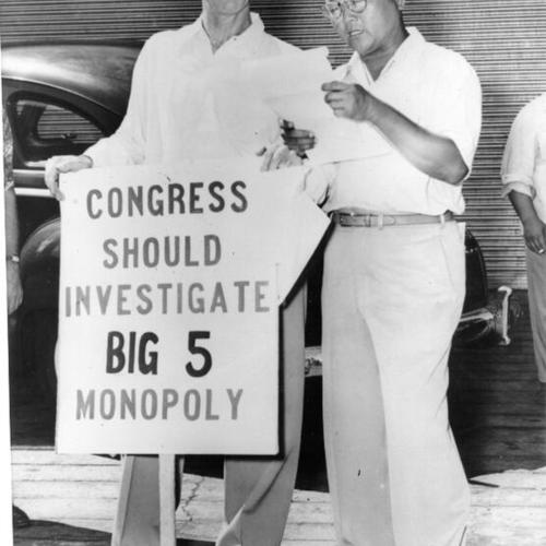 [Harry Bridges, ILWU president, pauses with his placard to listen to a deputy sheriff read court order prohibiting him from picketing]