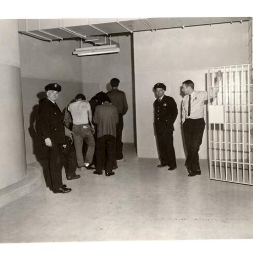 [Detainees with three officers, Pete Zelis (2nd from left), Frank G.[?] Leonard[?] in Old Hall of Justice]