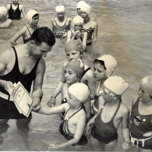[Paul H. Huedepohl, swimming instructor, handing out "Learn To Swim" diplomas to young swimmers at Sutro baths]