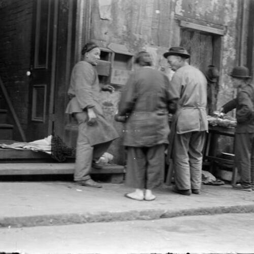 [Three men and one woman, chatting in front of mail boxes]