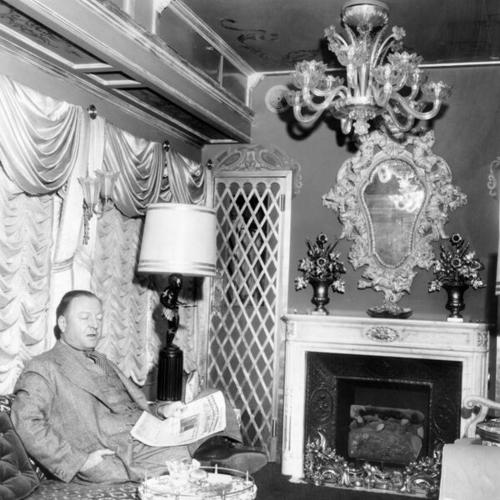 [Author Lucius Beebe perches comfortably on a divan in the drawing room of his luxurious new special car, fit for any Oriental potentate]