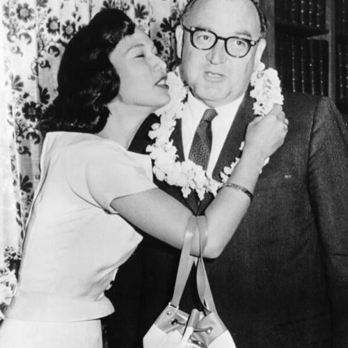 [Miss Hawaii gives Governor Brown the traditional island kiss after bedecking him with a lei of flowers]