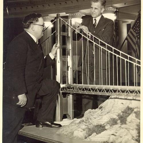 [Joseph Baermann Strauss, Chief Engineer of Golden Gate Bridge, and Supervisor Andrew Gallagher standing around the bridge model]