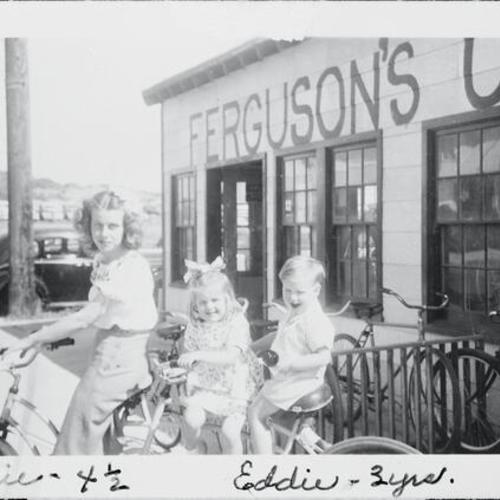 [Jane with her mother Mary and brother Eddie riding a tandem bicycle at Ferguson's Cyclery on Wawona Street]