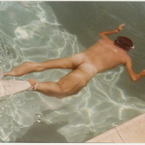 Daniel Detorie, nude, swimming in pool with swim fins at Rock Hudson's Palm Springs home